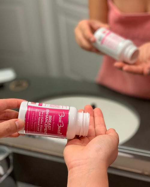 woman in front of a mirror taking Bust Bunny Breast Enhancement supplement