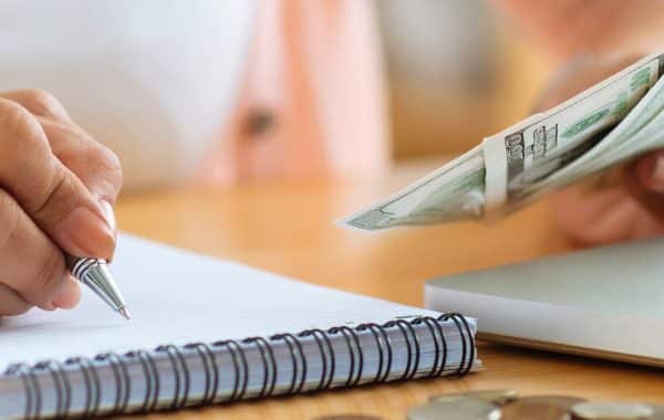 woman holding money while taking notes