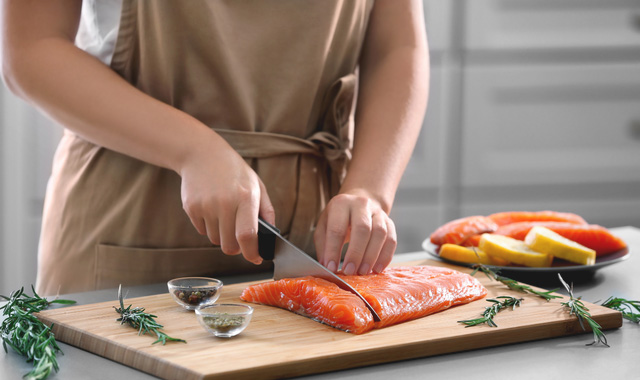 woman cutting fresh salmon fillet in kitchen